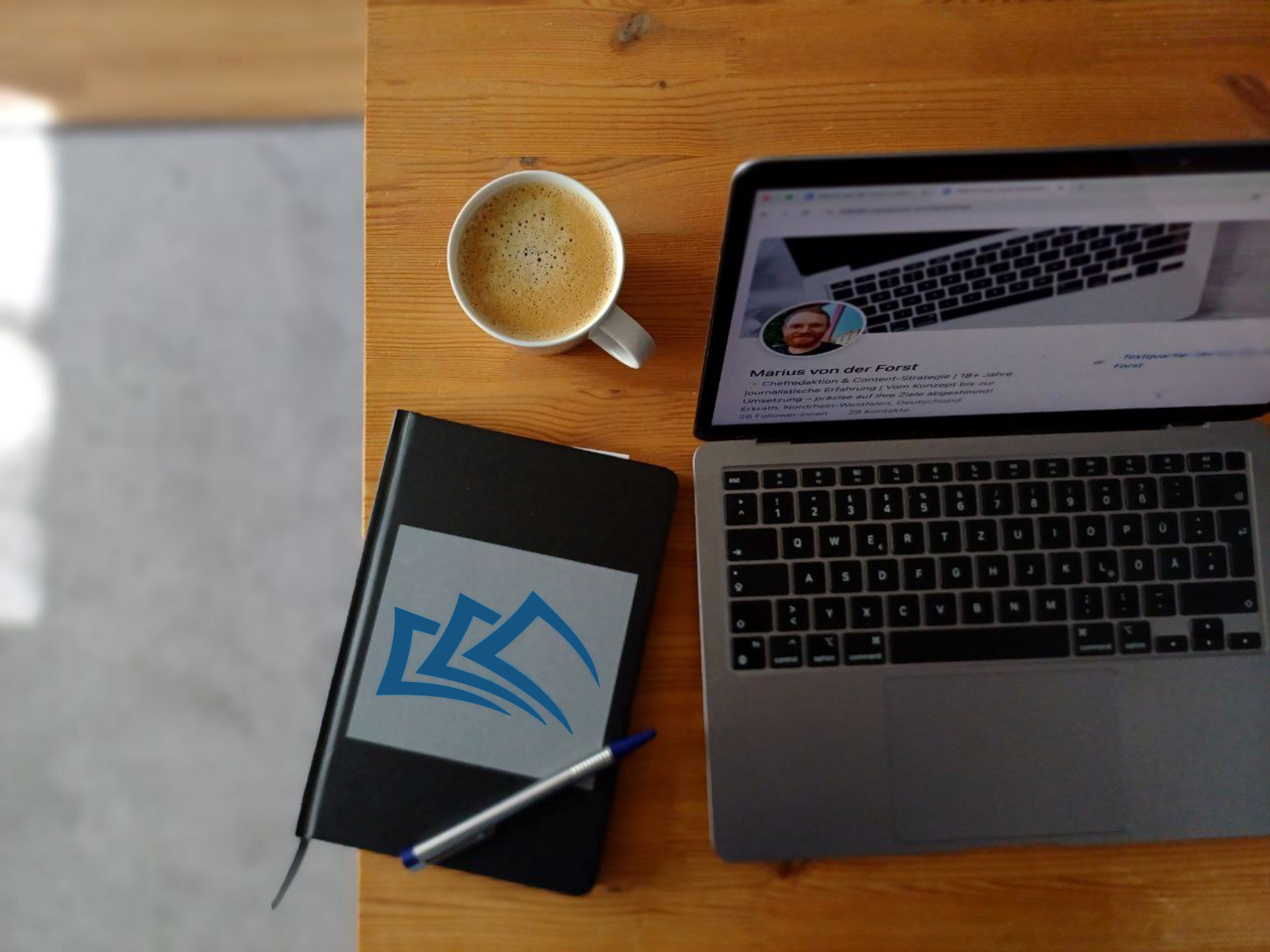 Laptop, Notizbuch und Kaffee auf einem Holztisch. Arbeitsplatz für Content-Strategie und Texterstellung beim Textquartier Marius von der Forst.