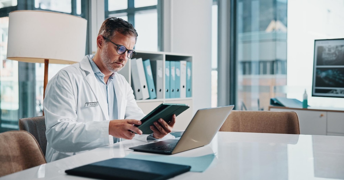 Arzt im Büro bei der Arbeit am Laptop und Tablet. Content-Marketing für Medizintechnik im Mittelstand durch das Textquartier Marius von der Forst.