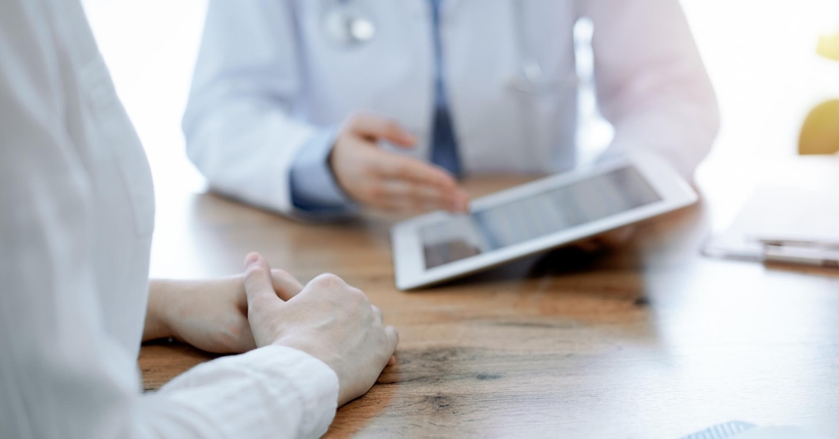 Zwei Personen im Gespräch, eine zeigt Informationen auf einem Tablet. Vier Ansätze zur Verbesserung der Gesundheitskommunikation im Blog des Textquartier Marius von der Forst.