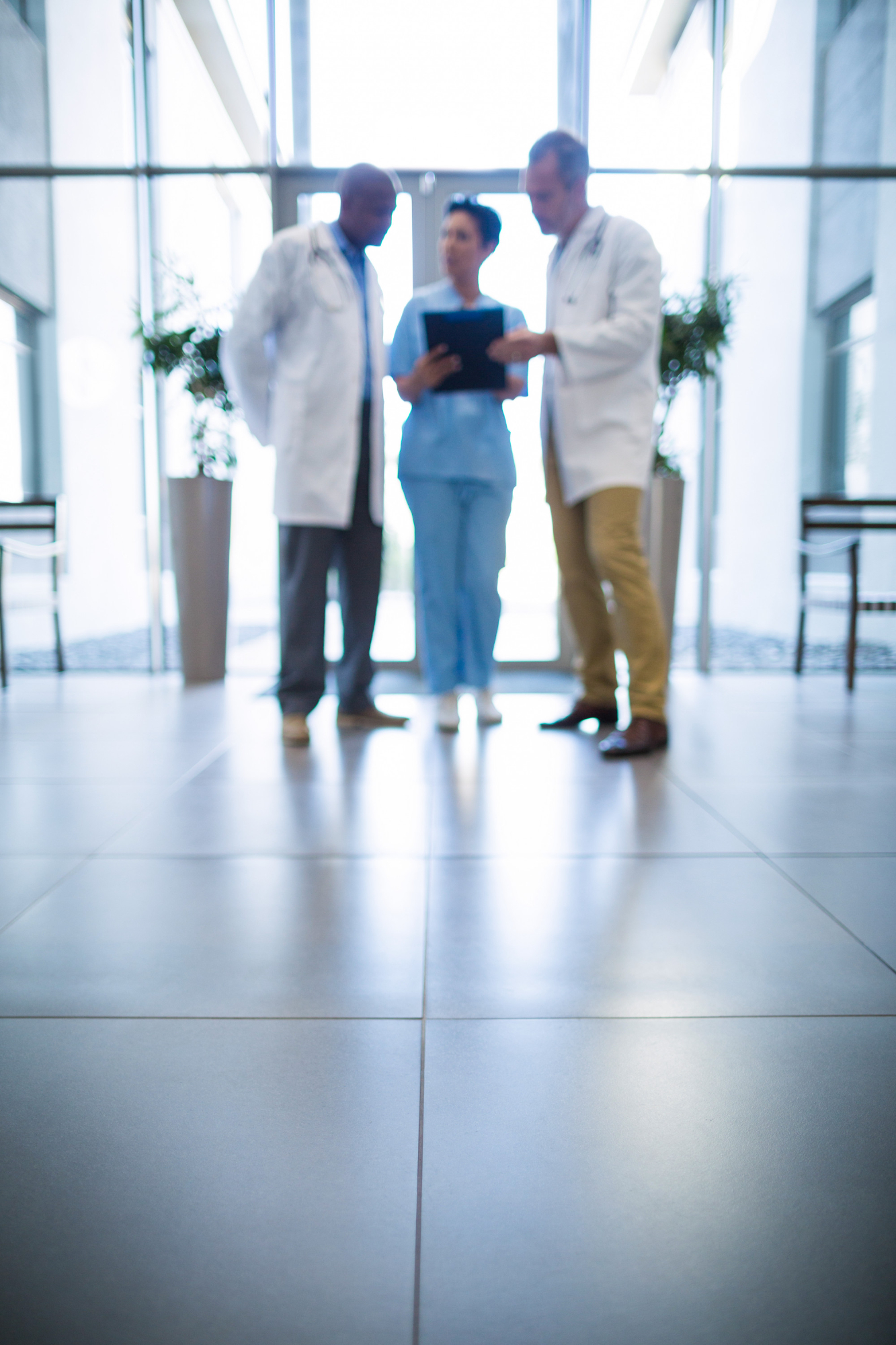 Drei medizinische Fachkräfte stehen in einem modernen Krankenhausflur und betrachten ein Tablet. Blogartikel über interne Gesundheitskommunikation vom Textquartier Marius von der Forst.