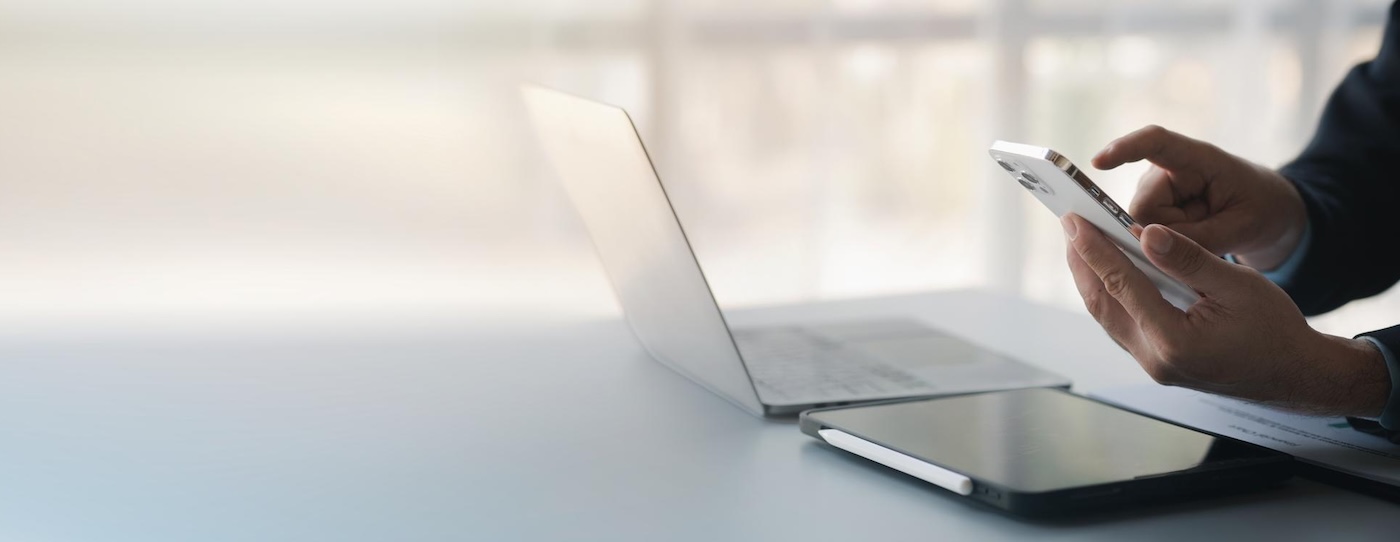 Person nutzt Smartphone und Laptop auf Schreibtisch. Marketing-Content beim Textquartier Marius von der Forst für IT- und Technologie-Branche.