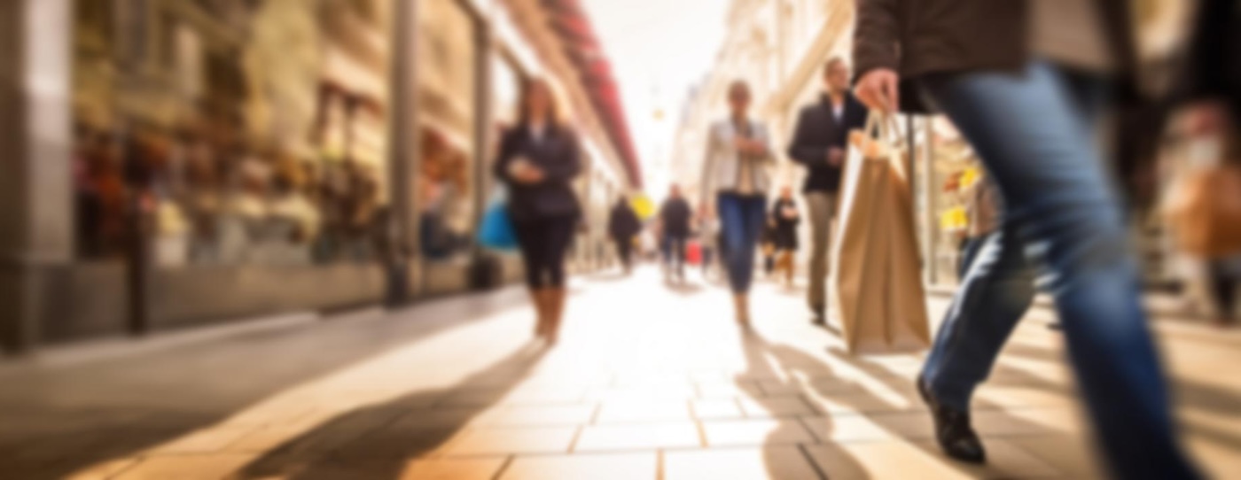 Menschen mit Einkaufstüten in sonniger Einkaufsstraße. Marketing-Texte und Copywriting für Konsumenten- und Verbraucherthemen beim Textquartier Marius von der Forst.