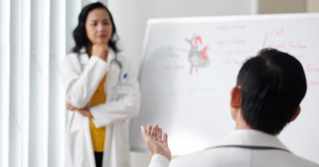 Ärzte diskutieren vor einem Whiteboard mit medizinischen Zeichnungen. Blogartikel über Herausforderungen in Gesundheitskommunikation vom Textquartier Marius von der Forst.